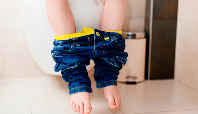 Foto: Kleines Kind sitzt auf der Toilette. Es sind nur die Beine zu sehen.