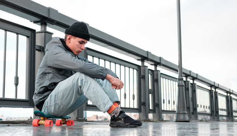 Foto: Trauriger Teenager Junge sitzt auf seinem Skateboard.