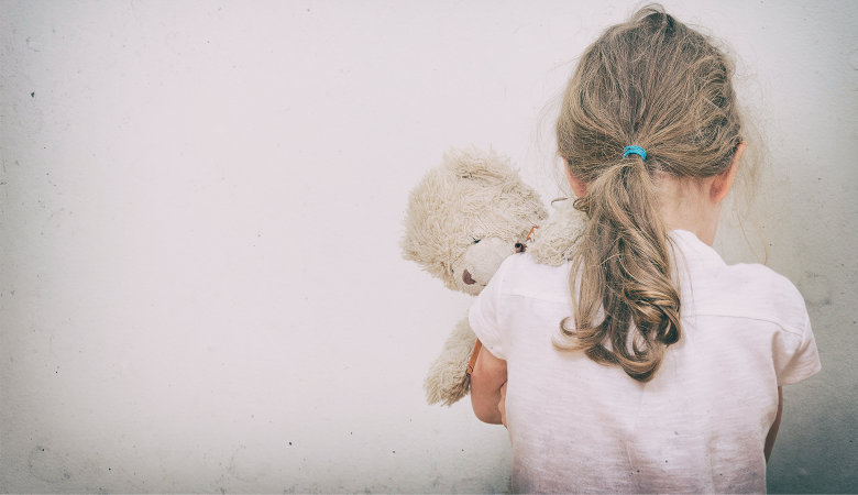 Foto: Kleines Mädchen mit Teddy auf dem Arm steht zur Wand und weint