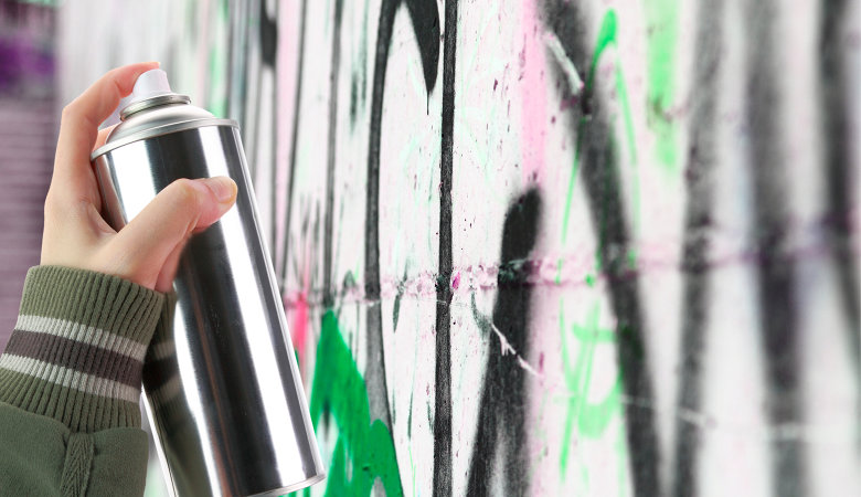 Foto: Eine Hand mit einer Spraydose, die auf eine Grafitti Wand sprüht.
