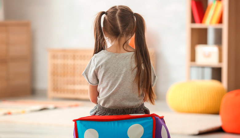 Foto: Kleines Mädchen sitzt mit dem Rücken zur Kamera im Kinderzimmer auf einem Hocker