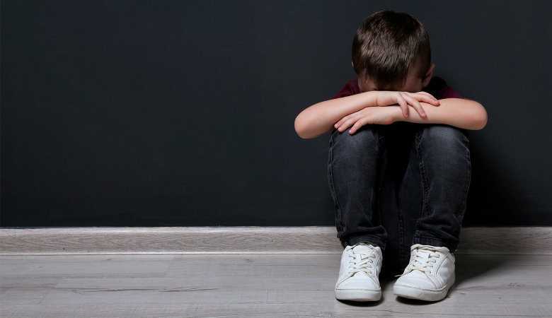 Foto: Trauriger kleiner Junge sitzt in der Hocke auf dem Fußboden und verschränkt seine Arme vor dem Gesicht