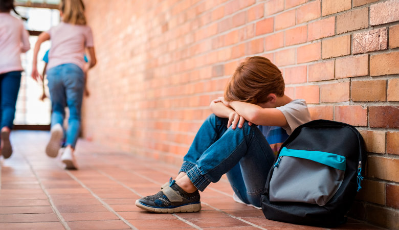 Foto: Kleiner Schuljunge sitzt in der Schule am Boden und ist traurig