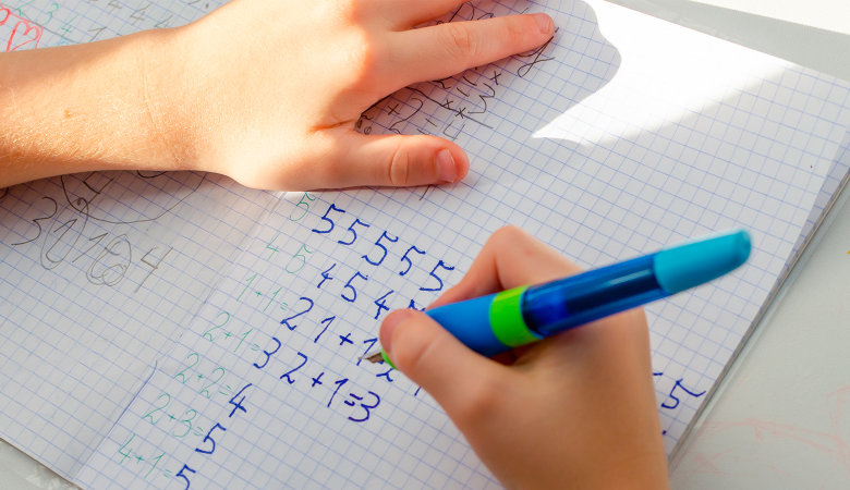 Foto: Nahaufnahme Kind, welches Mathe-Aufgaben in ein Heft schreibt.