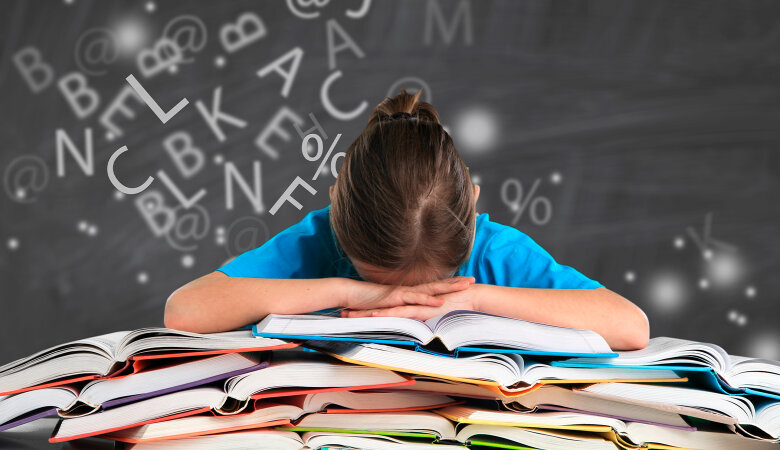 Foto: Schulmädchen sitz am Schreibtisch und hat Kopf auf den Armen und auf einen Stapel Bücher aufgelegt.