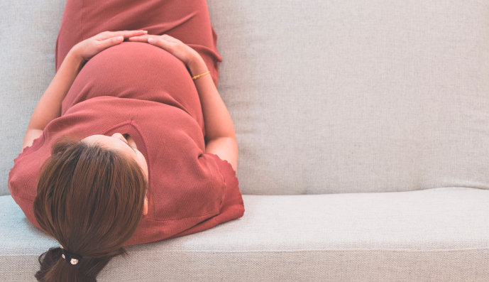 Foto: Schwangere Frau sitzt auf grauem Sofa