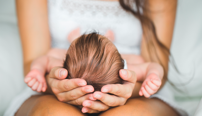 Foto: Mutter, die den Kopf ihres neugeborenen Sohnes in Händen hält.