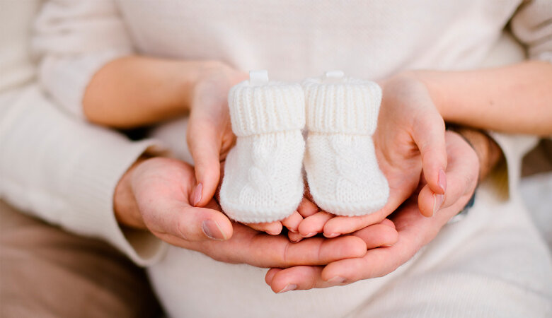 Foto: Ineinanderliegende Männer- und Frauenhände die Babyschuhe aus Wolle halten