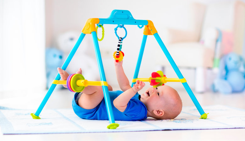 Foto: Baby liegt auf dem Rücken unter einem Spielgerät und greift nach den herunterhängenden Spielsachen