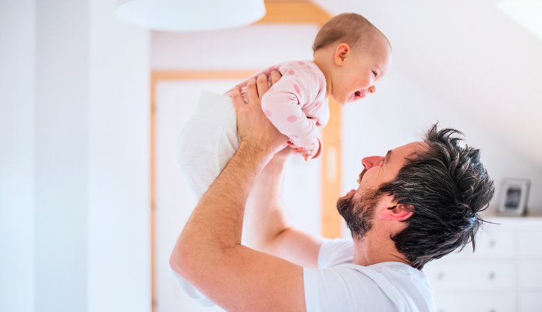 Foto: Lachender Vater hält lachendes Baby mit beiden Armen in die Höhe